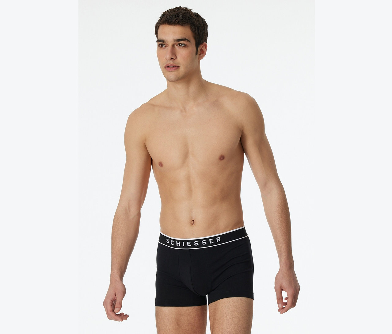 Mężczyzna pozuje bez koszulki w czarnych bokserkach marki Schiesser.