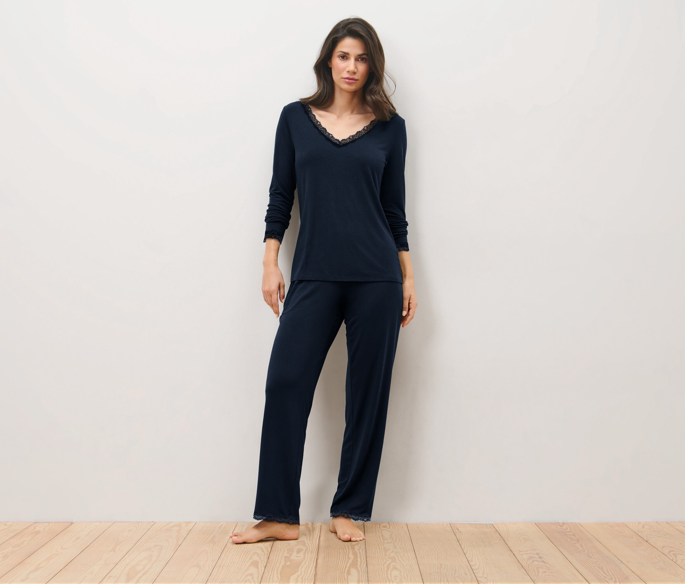 Kobieta stoi na drewnianej podłodze w granatowej piżamie.