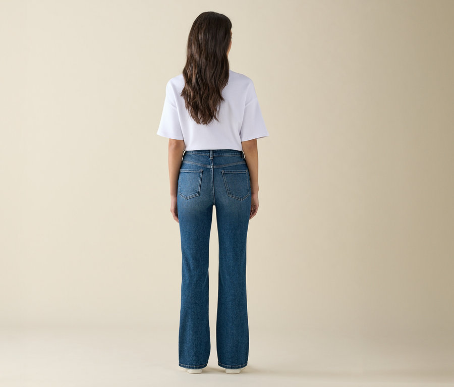 Kobieta z długimi brązowymi włosami stoi tyłem do kamery, ubrana w białą koszulkę i niebieskie dżinsy.