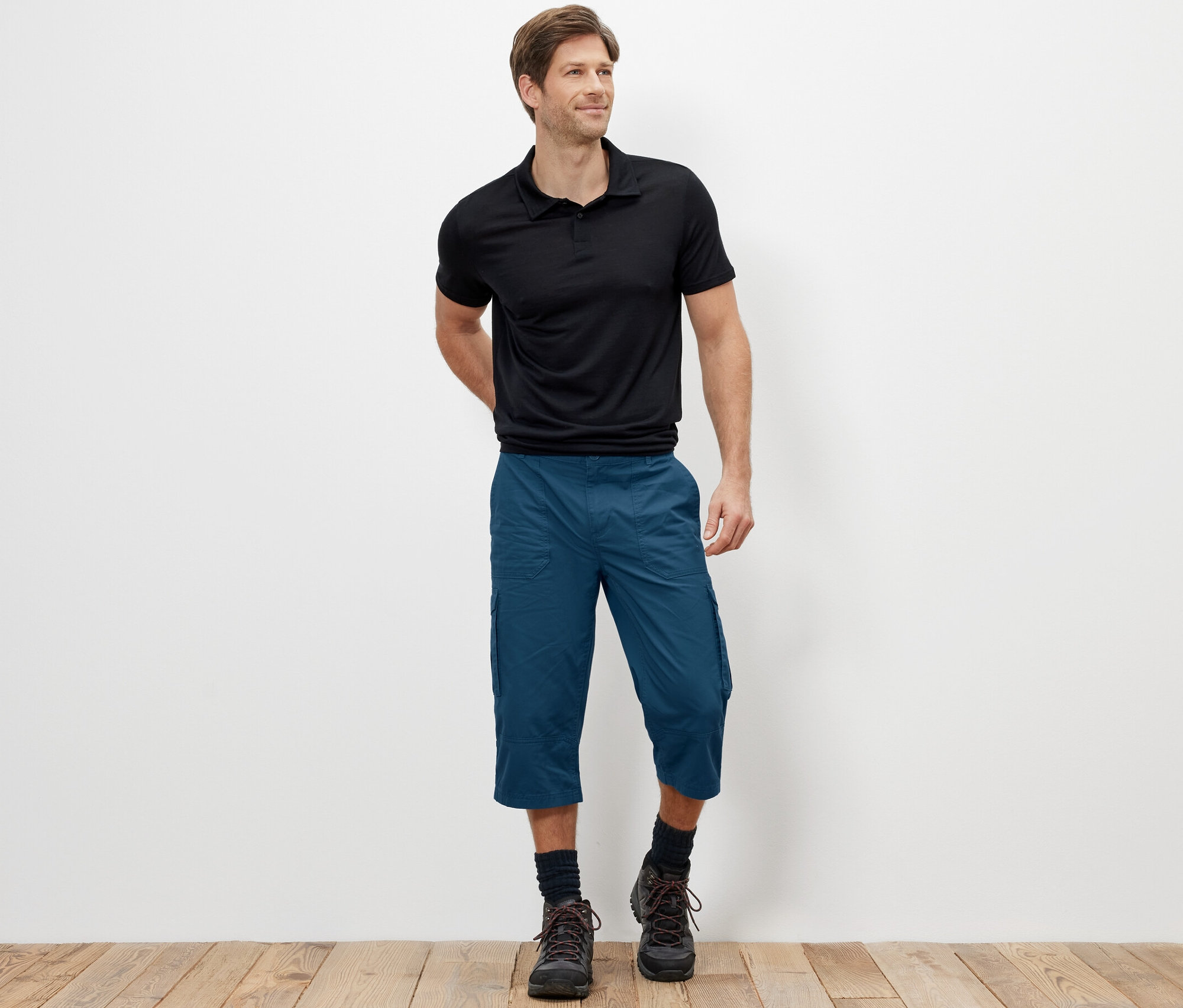 Mężczyzna stoi i ma na sobie niebieskie bermudy bojówki o długości 3/4.