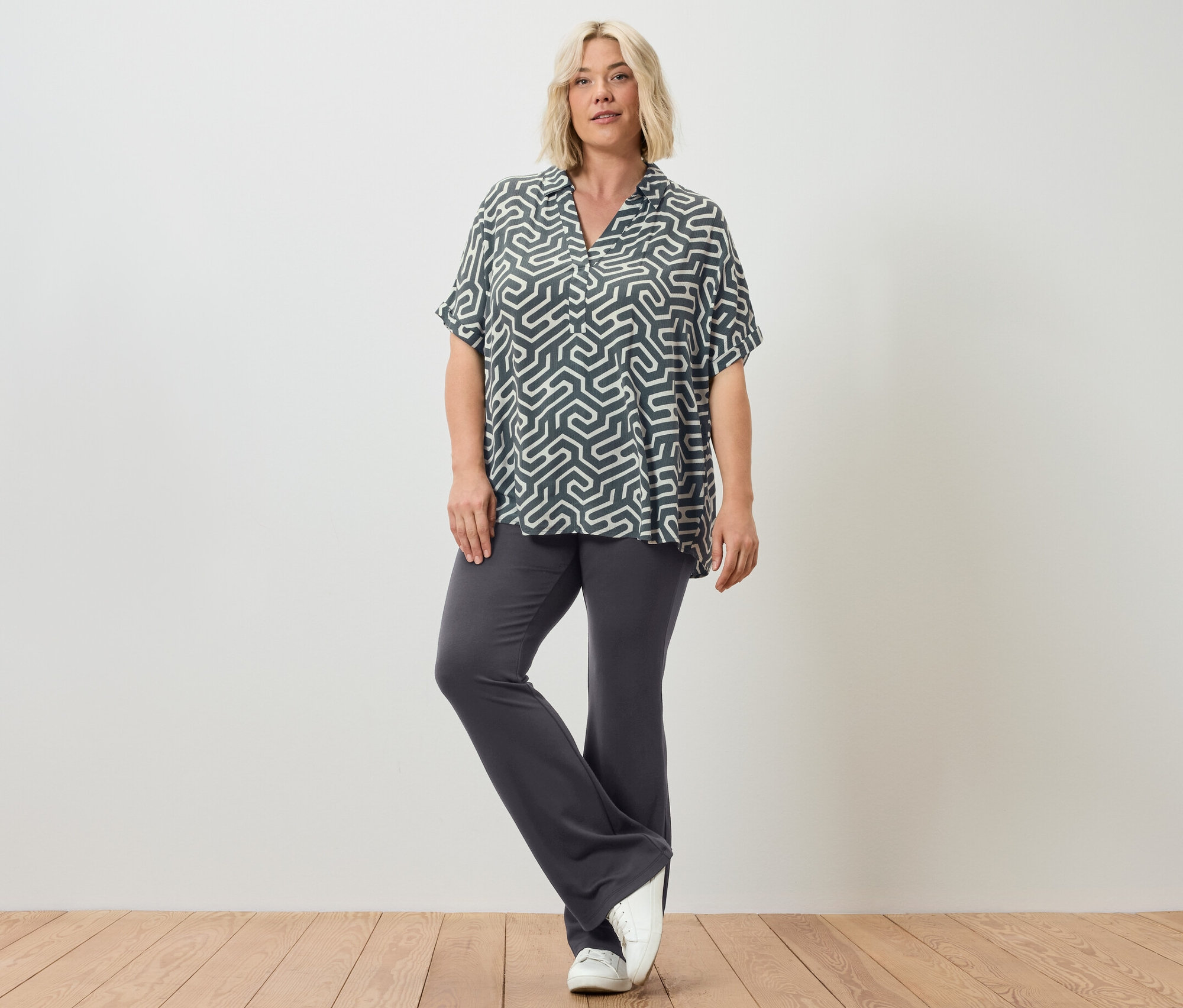 Kobieta pozuje w rozszerzanych legginsach i wzorzystej bluzce.