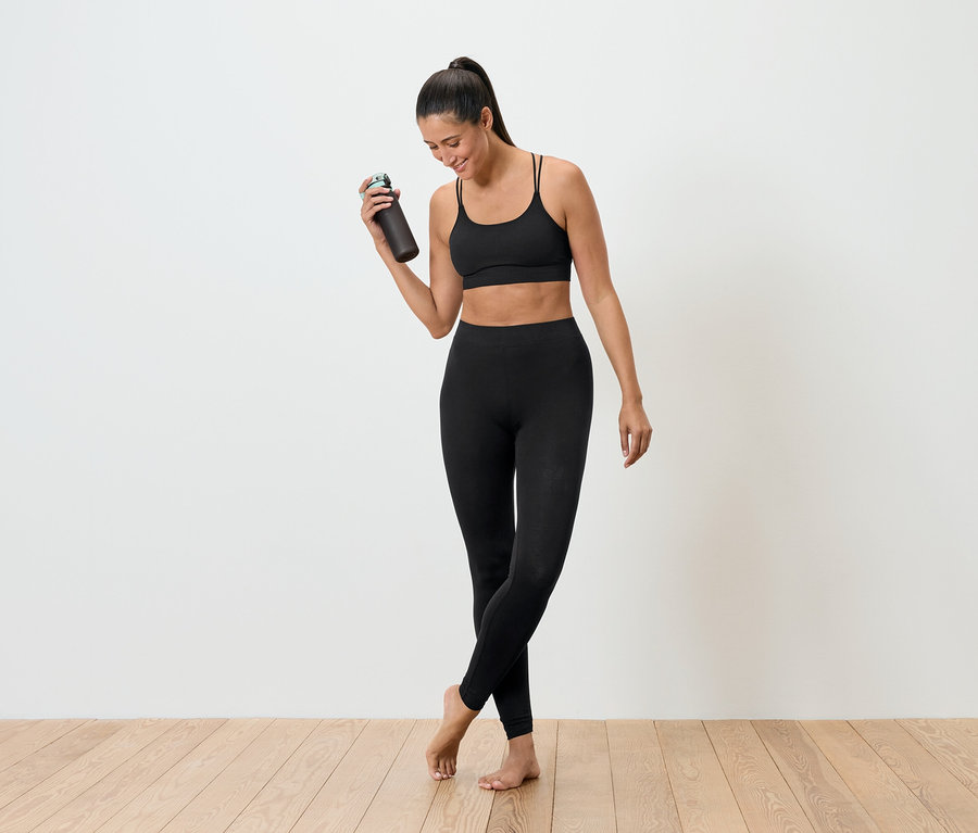Kobieta w czarnym stroju sportowym trzyma butelkę z wodą.
