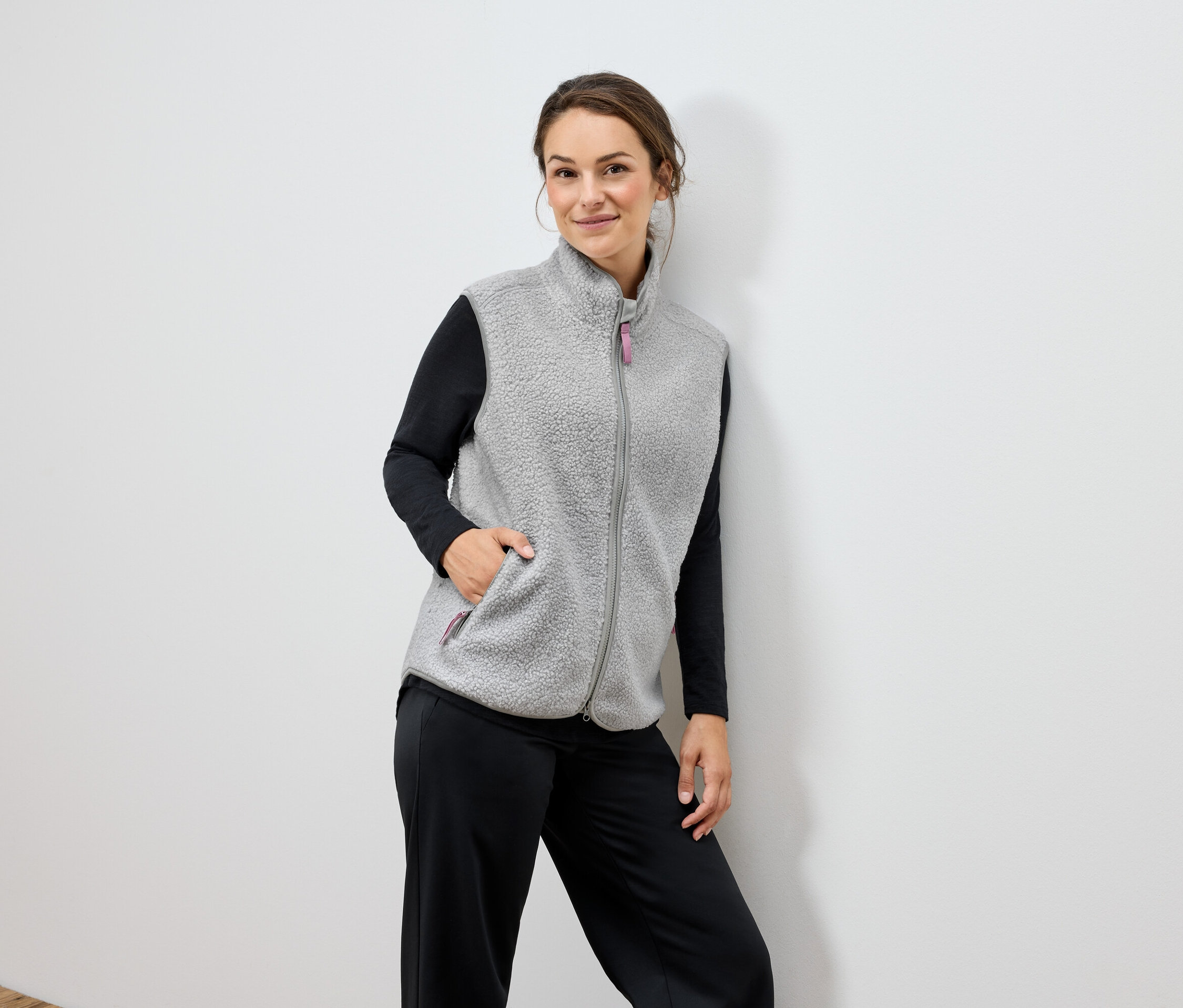 Kobieta ma na sobie szarą kamizelkę polarową i czarne spodnie.