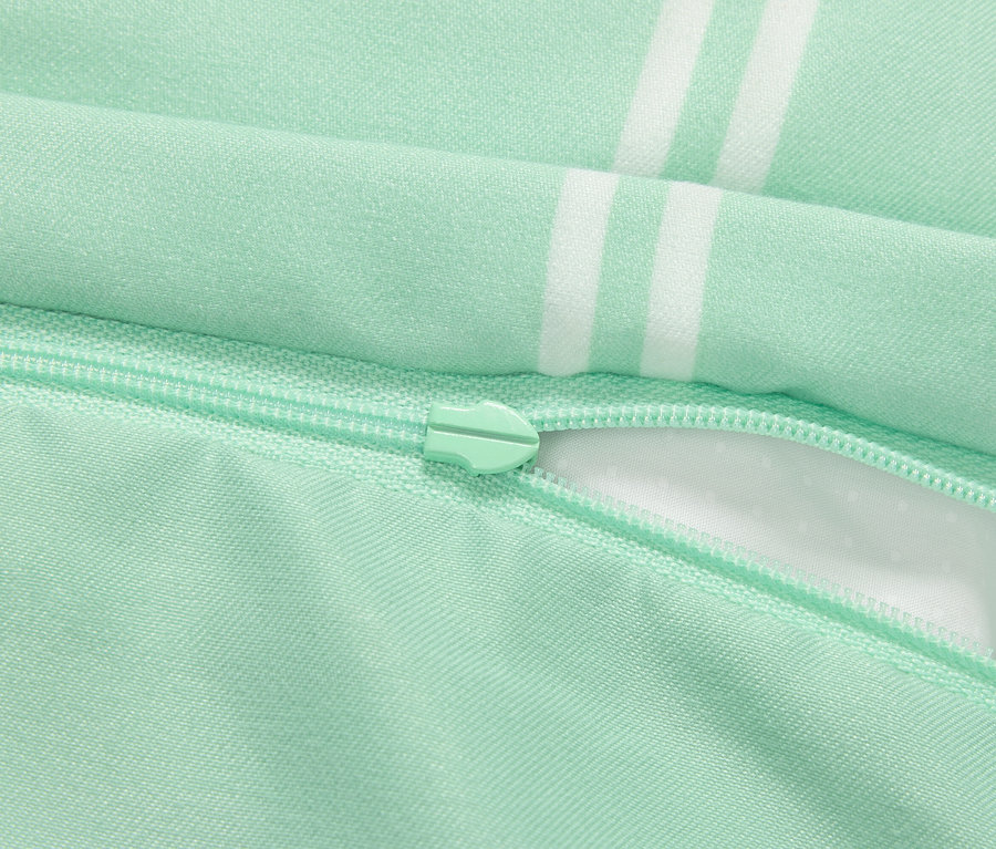 Szczegół jasnozielonej poszewki na poduszkę z zamkiem błyskawicznym i białymi paskami.