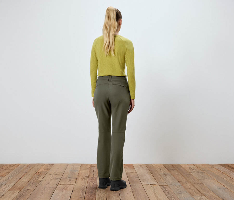 Kobieta stoi tyłem do kamery, ubrana w zielone spodnie i żółtą bluzkę.
