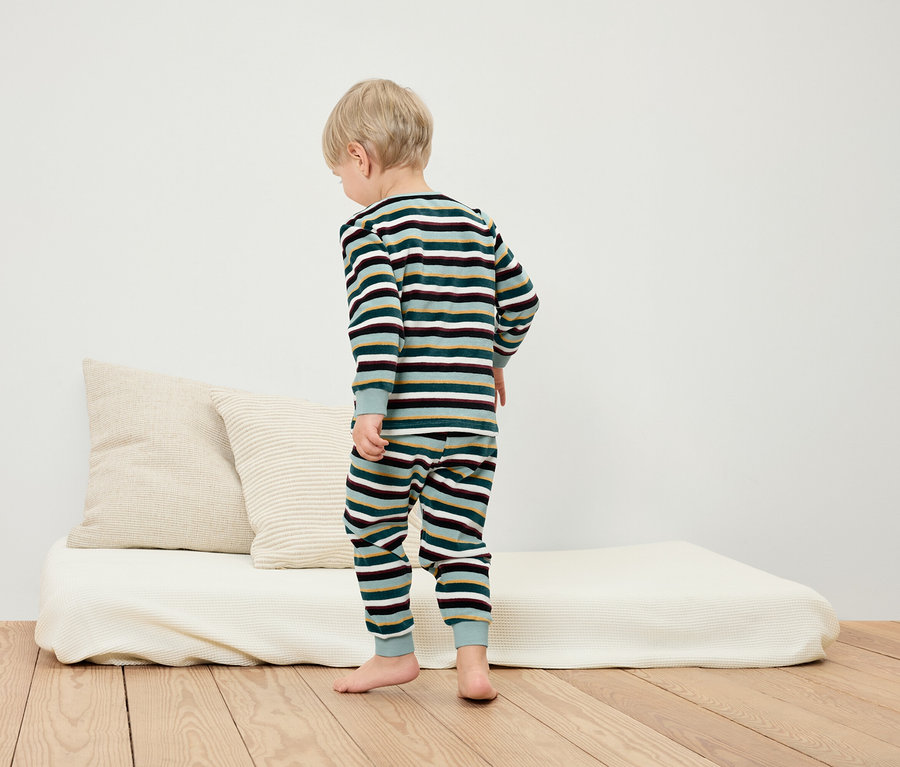 Chłopiec stoi na podłodze w piżamie w paski obok białego łóżka i poduszek.