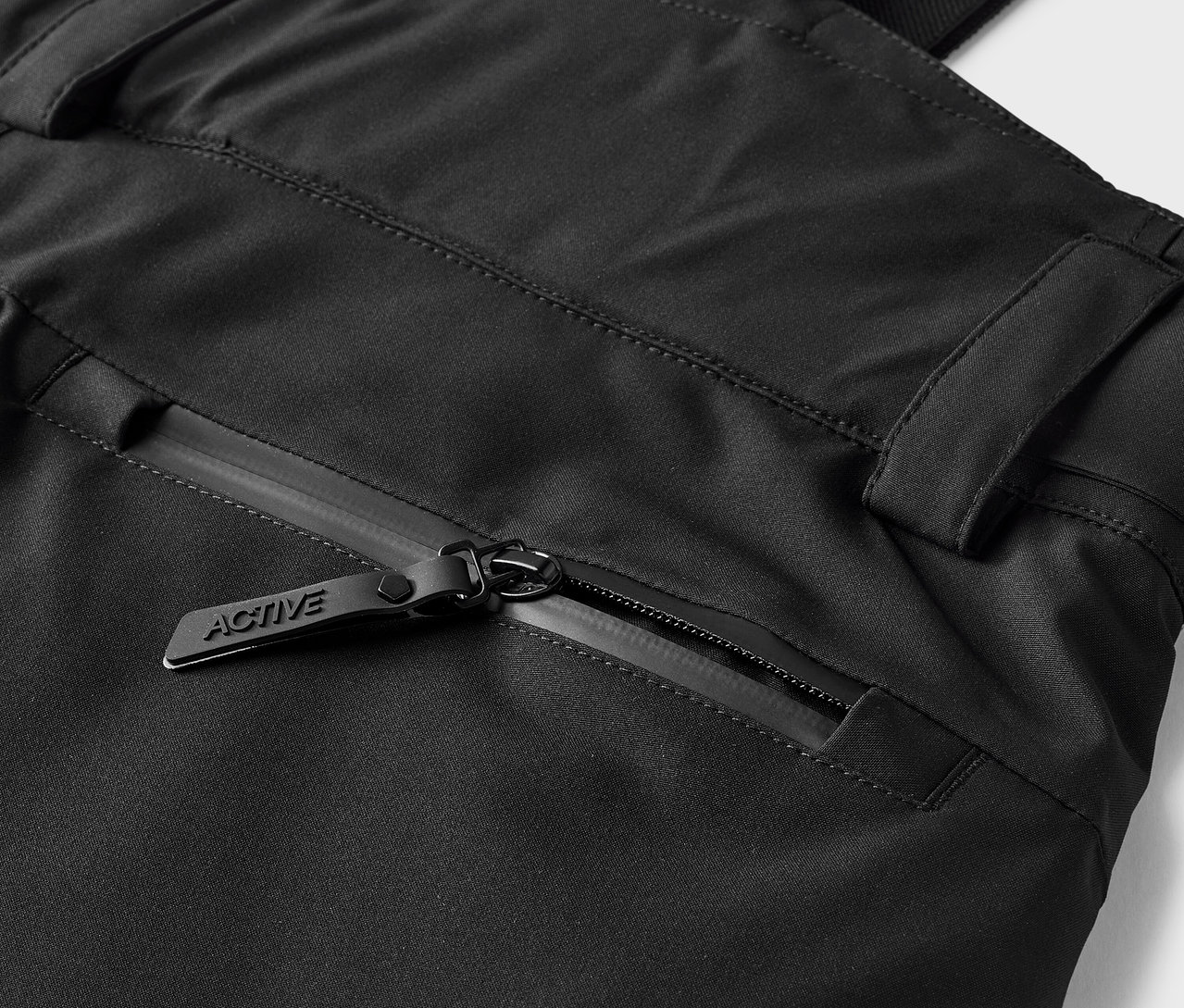 Szczegół czarnych spodni z kieszenią na zamek błyskawiczny i suwakiem z napisem ACTIVE.