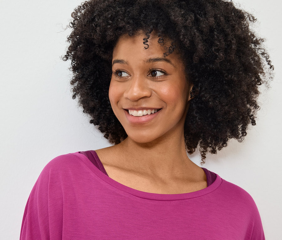 Portret uśmiechniętej kobiety z fryzurą afro w różowej koszulce.