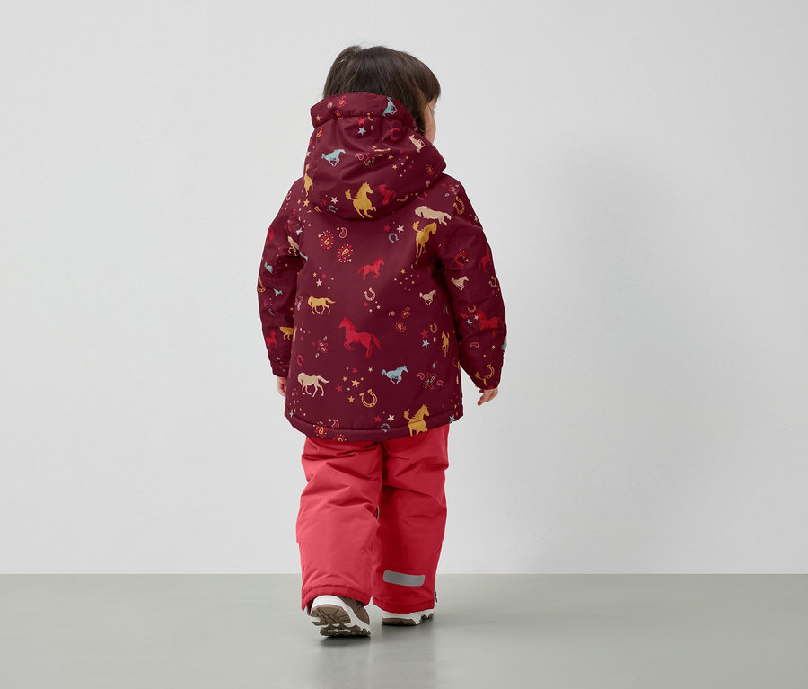 Chłopiec w zimowej kurtce z nadrukiem koni i czerwonych spodniach, tyłem do kamery.
