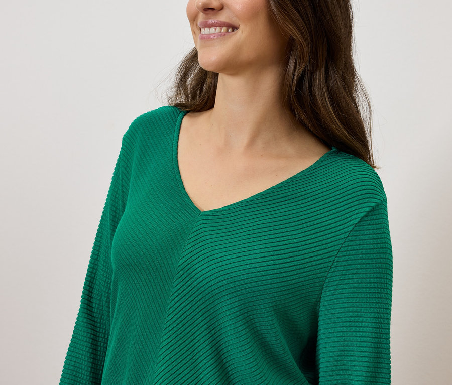 Uśmiechnięta brunetka w zielonym swetrze z dekoltem w serek.