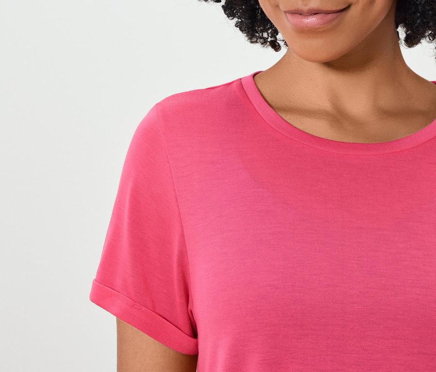 Górna część ciała kobiety o ciemnych włosach w różowej koszulce z krótkim rękawem.