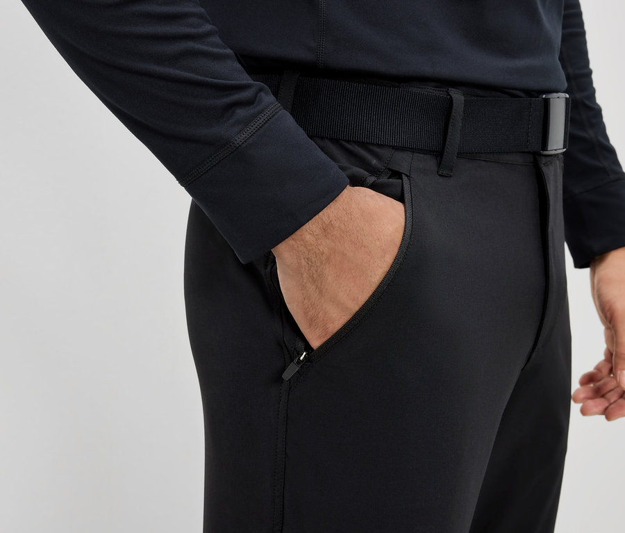 Mężczyzna trzyma rękę w kieszeni czarnych spodni z paskiem.