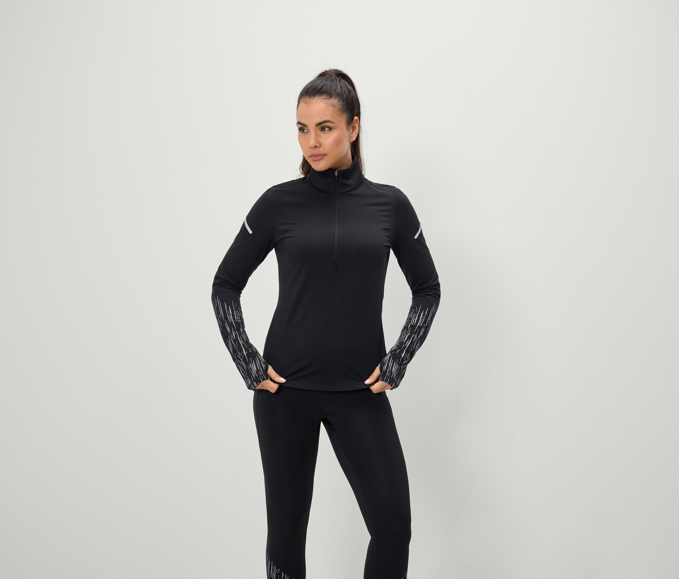 Kobieta pozuje w czarnym stroju sportowym z długim rękawem i legginsami.