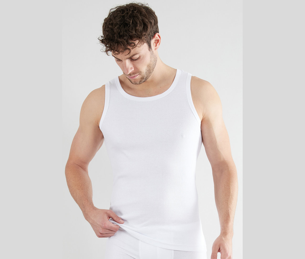 Mężczyzna nosi białą koszulkę na ramiączkach z prążkami i slipy.