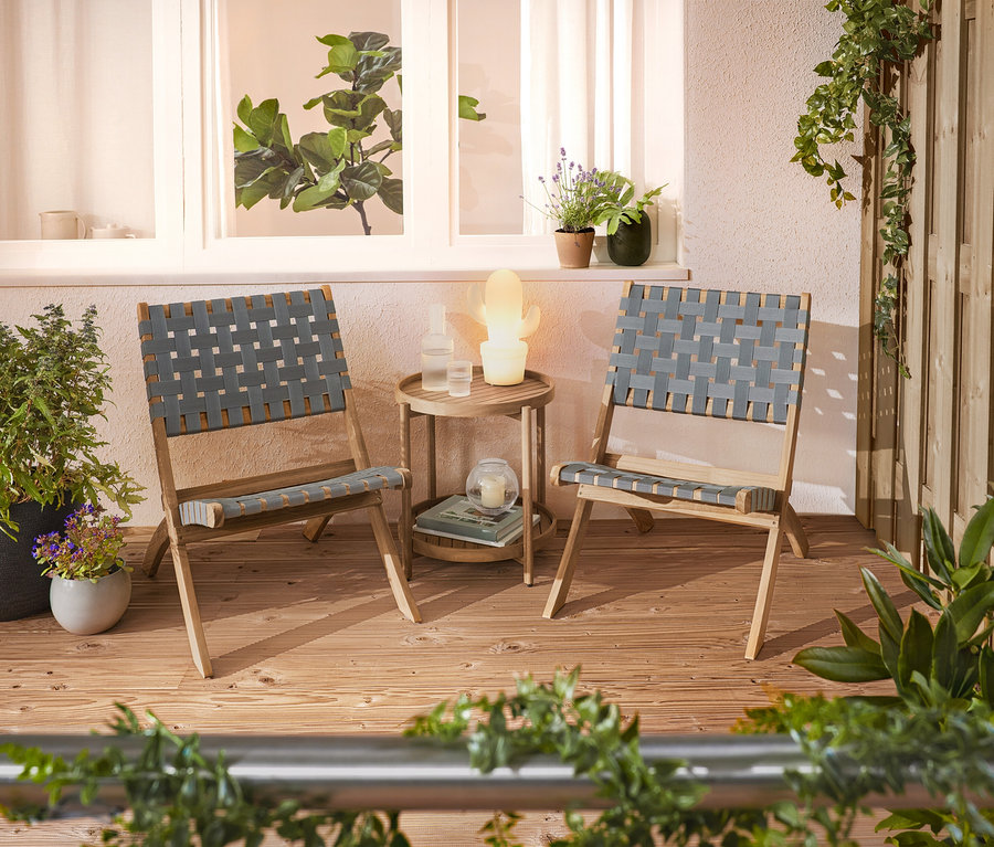 Dwa plecione krzesła i stolik pomocniczy stoją na tarasie.
