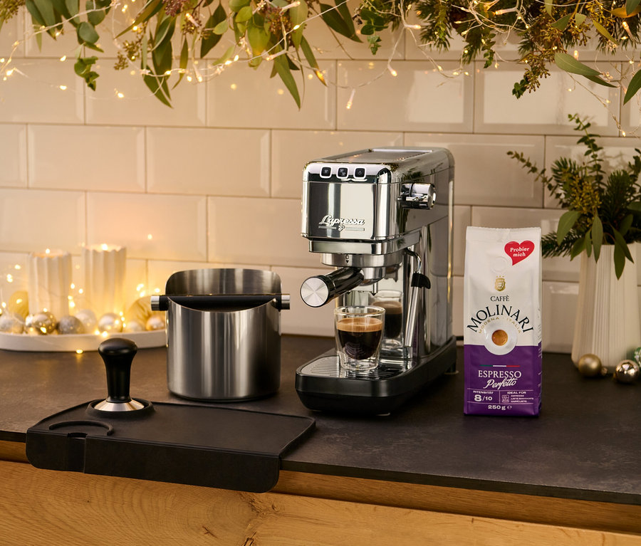 Na blacie kuchennym stoi srebrny ekspres kolbowy do kawy »Lapressa« obok filiżanki espresso.