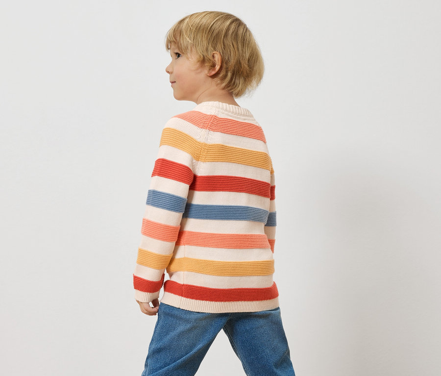 Dziecko o blond włosach ma na sobie pasiasty sweter i dżinsy na białym tle.