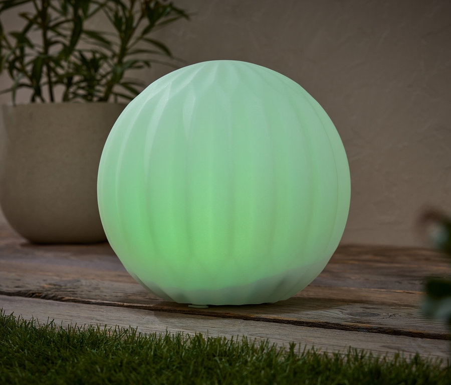 Zielona, kulista lampa stoi na drewnianej powierzchni obok rośliny doniczkowej.