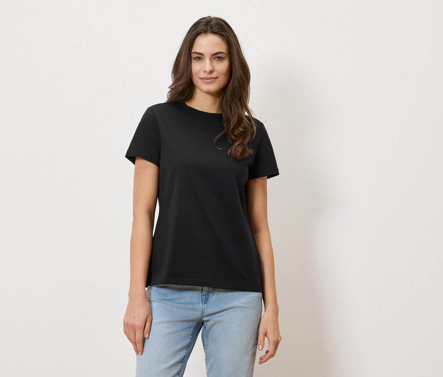 Kobieta o falowanych włosach ma na sobie czarny T-shirt i dżinsy.