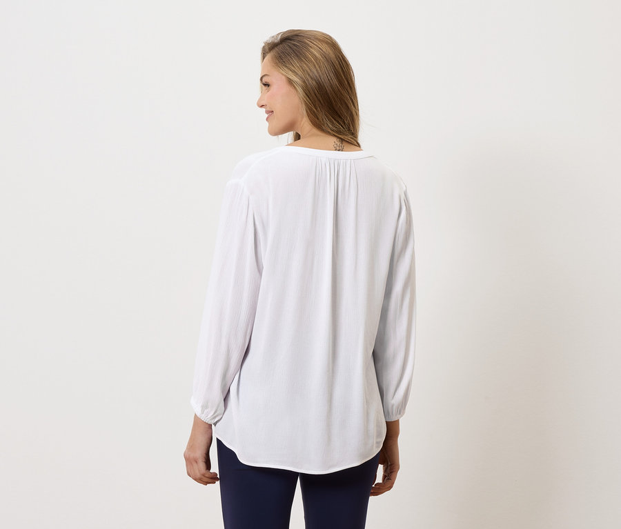 Kobieta od tyłu, ubrana w długą, białą bluzkę i niebieskie spodnie.