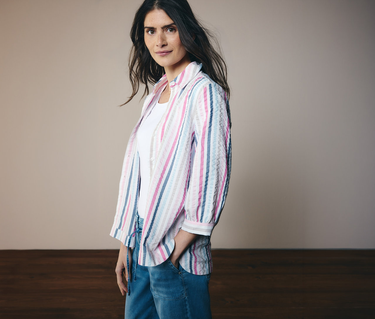Kobieta w bluzce koszulowej CECIL w paski z rękawami 3/4 i dżinsach. Jedną rękę trzyma w kieszeni.