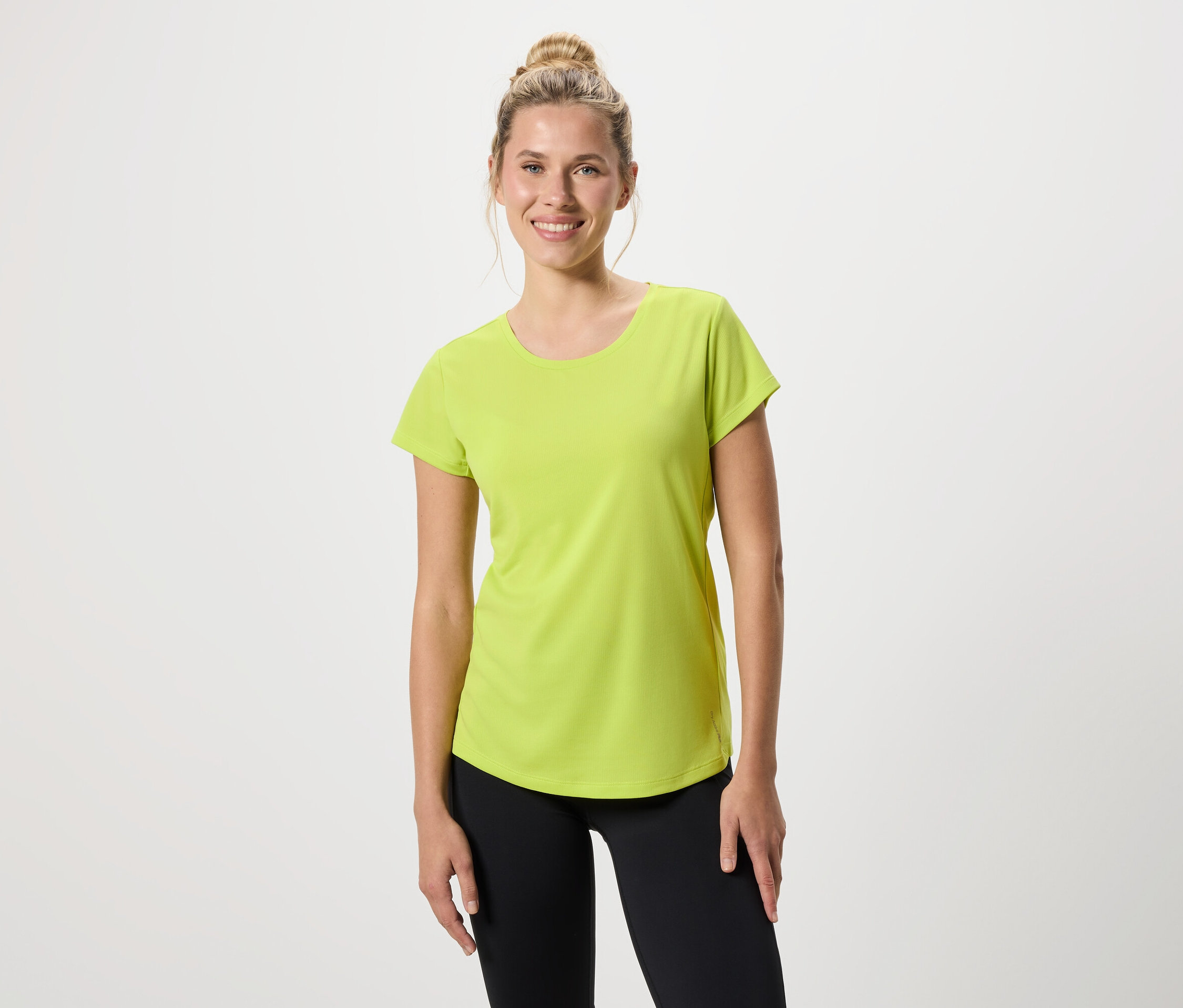 Kobieta ma na sobie jasnozieloną koszulkę i czarne legginsy.