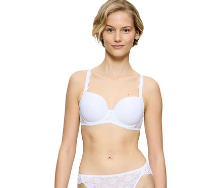 Kobieta z krótkimi blond włosami w białym biustonoszu Triumph Amourette WP i pasujących białych koronkowych figach, na białym tle.