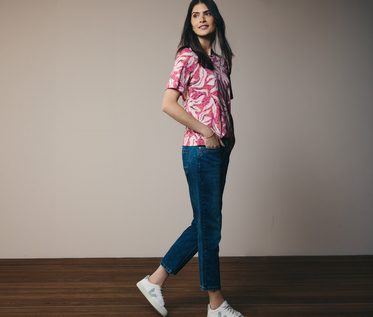 Kobieta idzie w różowej koszulce z krótkim rękawem CECIL i dżinsach. Ręce ma w kieszeniach.