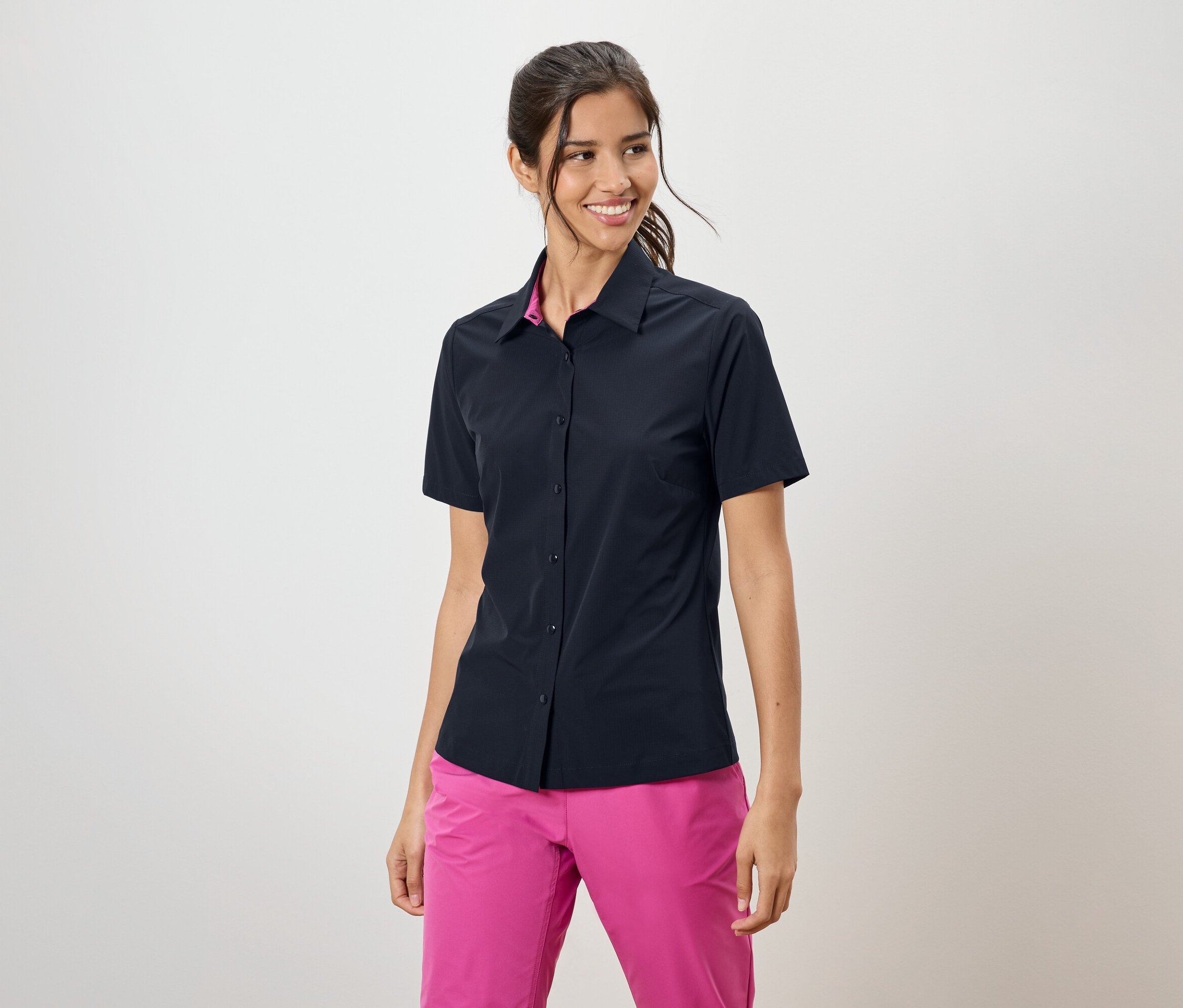Kobieta ma na sobie granatową koszulę z krótkim rękawem i różowe spodnie.