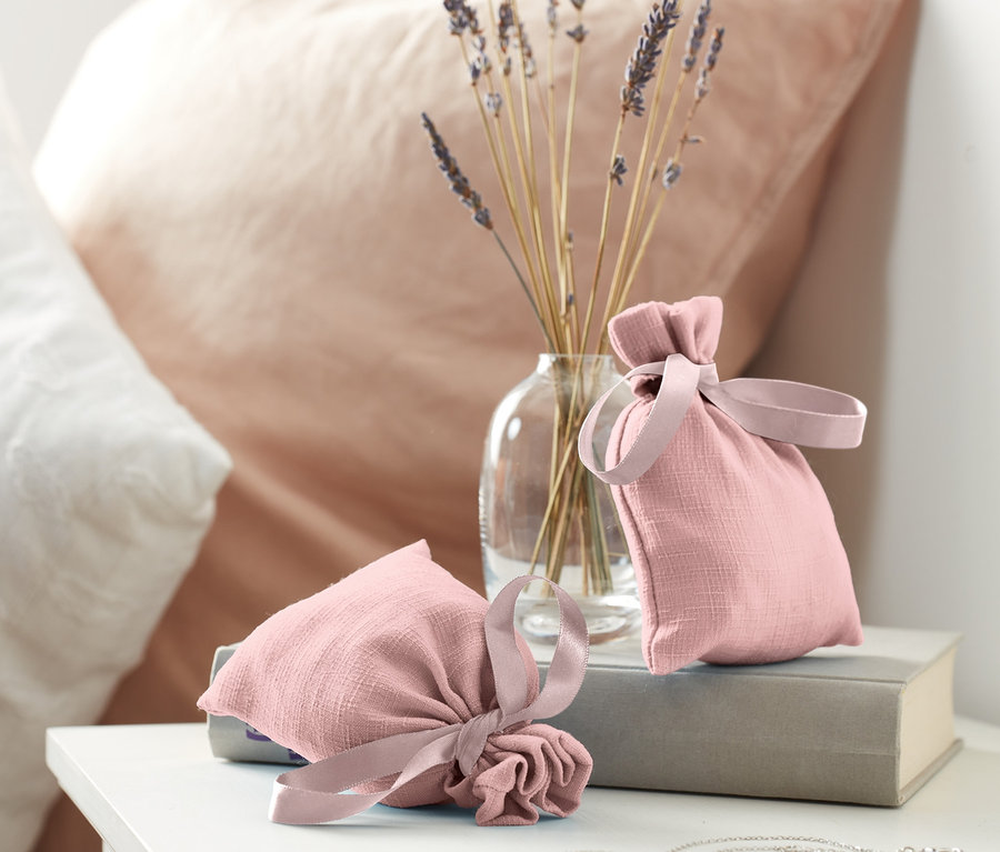Dwa woreczki zapachowe leżą na książce obok wazonu z lawendą.