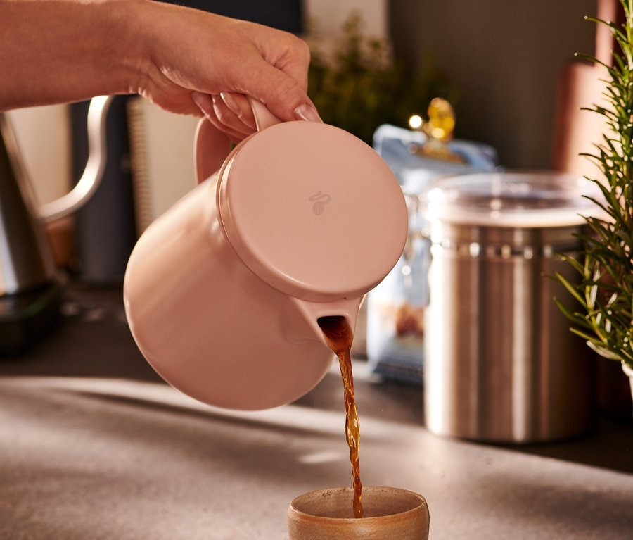 Ręka nalewa kawę z różowego, ceramicznego zaparzacza do kawy do filiżanki.