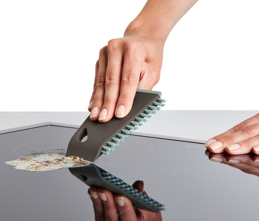 Ręka czyści płytę ceramiczną uniwersalną szczotką kuchenną.