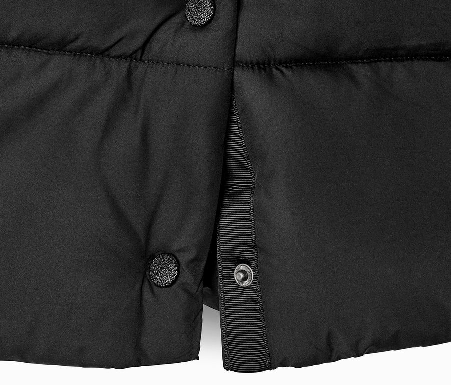 Detalle czarnego płaszcza pikowanego z kapturem i guzikami.