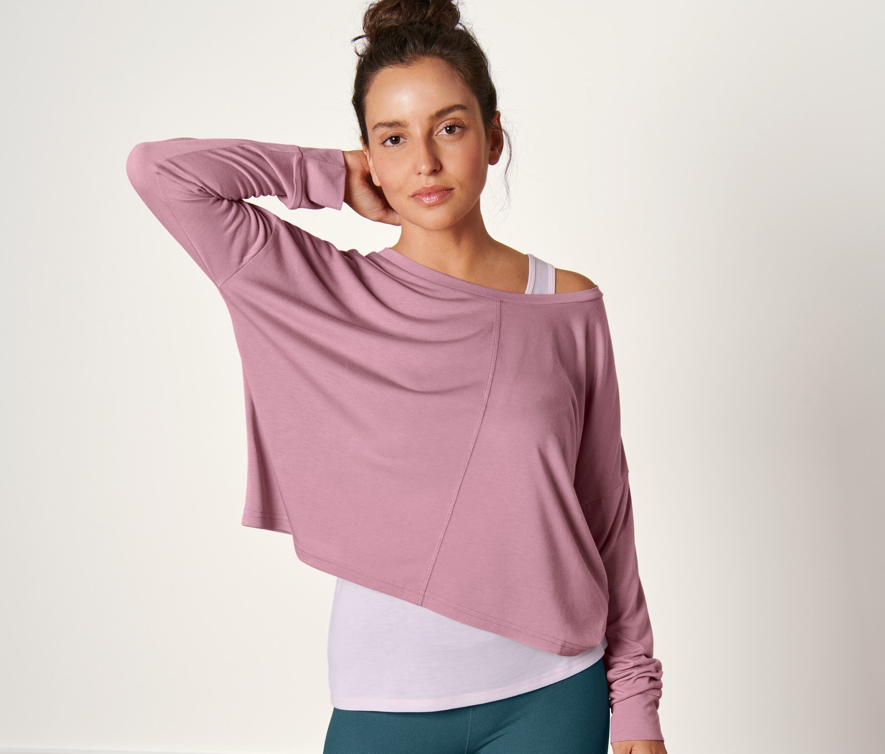 Kobieta pozuje w różowej koszulce sportowej 2 w 1 i zielonych legginsach.