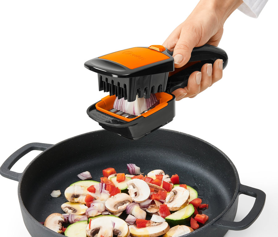 Ręka używa krajalnicy Nicer Dicer Quick XXL do krojenia cebuli nad patelnią z warzywami.