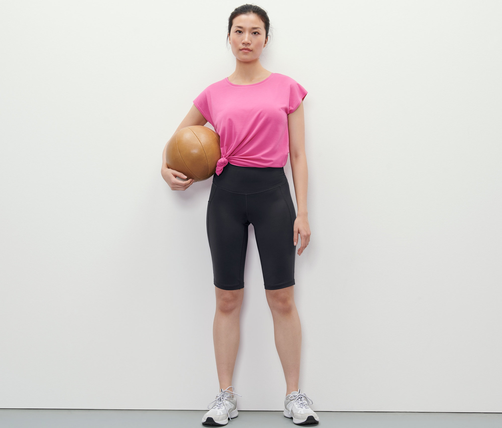 Kobieta trzyma piłkę lekarską i ma na sobie krótkie legginsy.