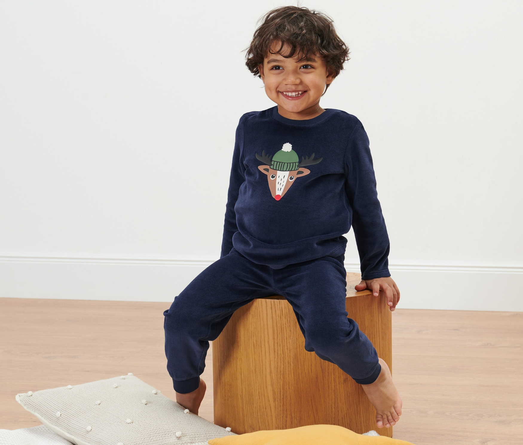 Chłopiec siedzi na drewnianym klocku, ubrany w piżamę z weluru dziecięcą.