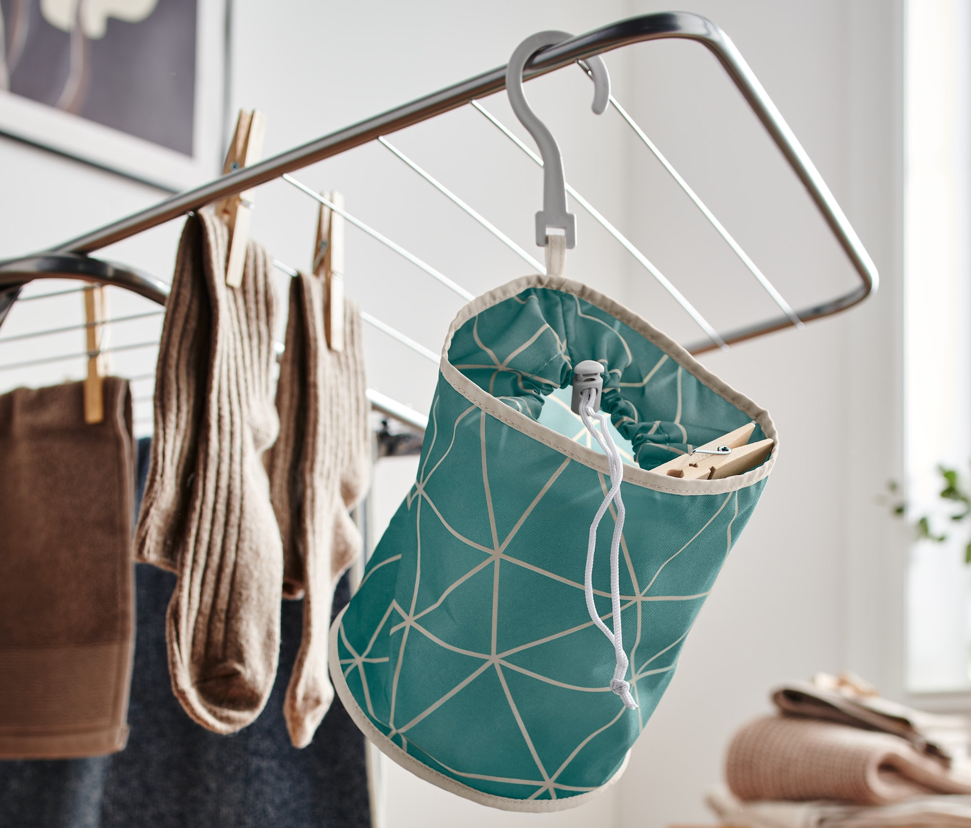 Worek na klamerki do bielizny w zielone wzory wisi na suszarce.