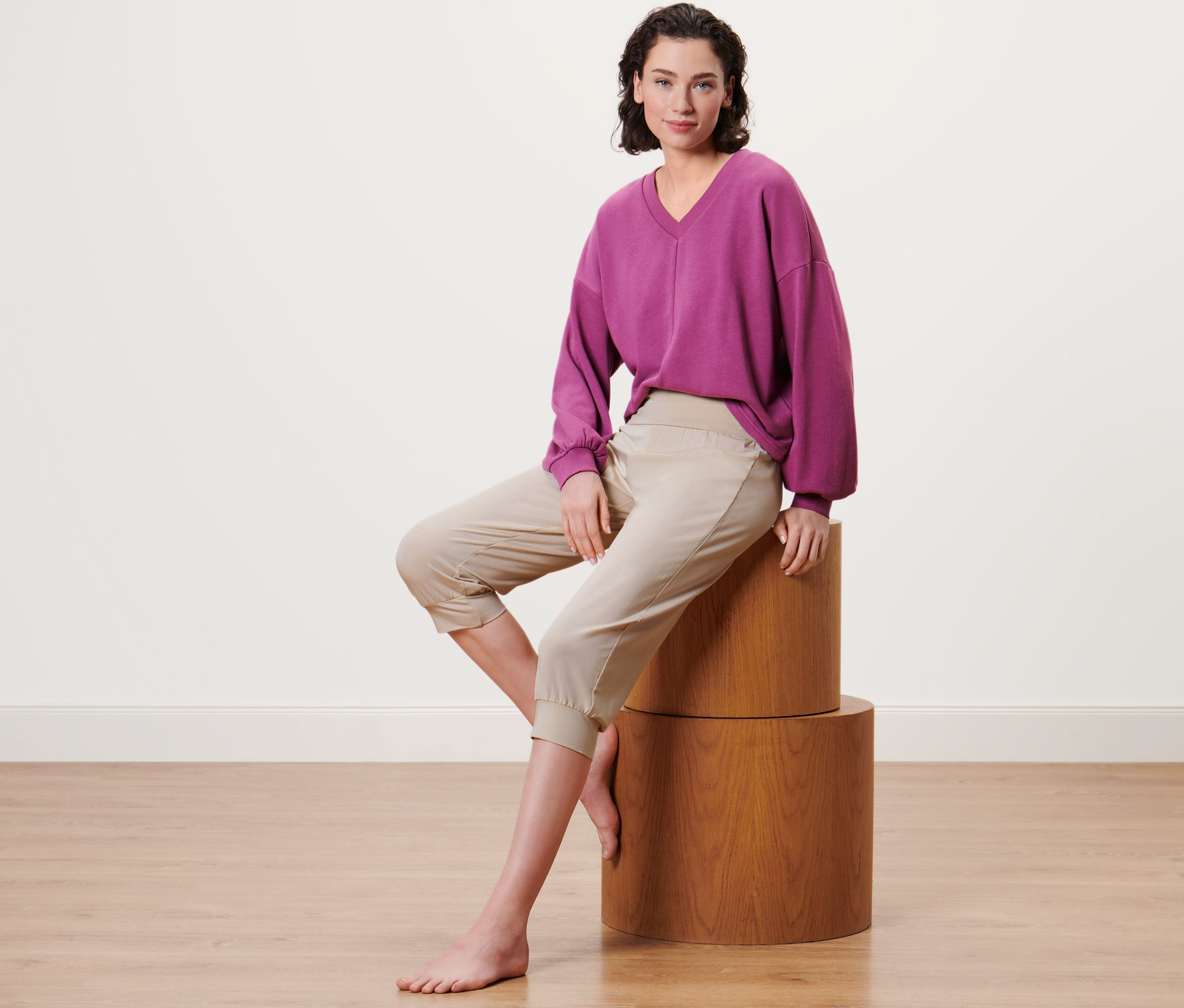 Kobieta siedzi na drewnianym cokole i ma na sobie beżowe spodnie do jogi o długości 3/4.