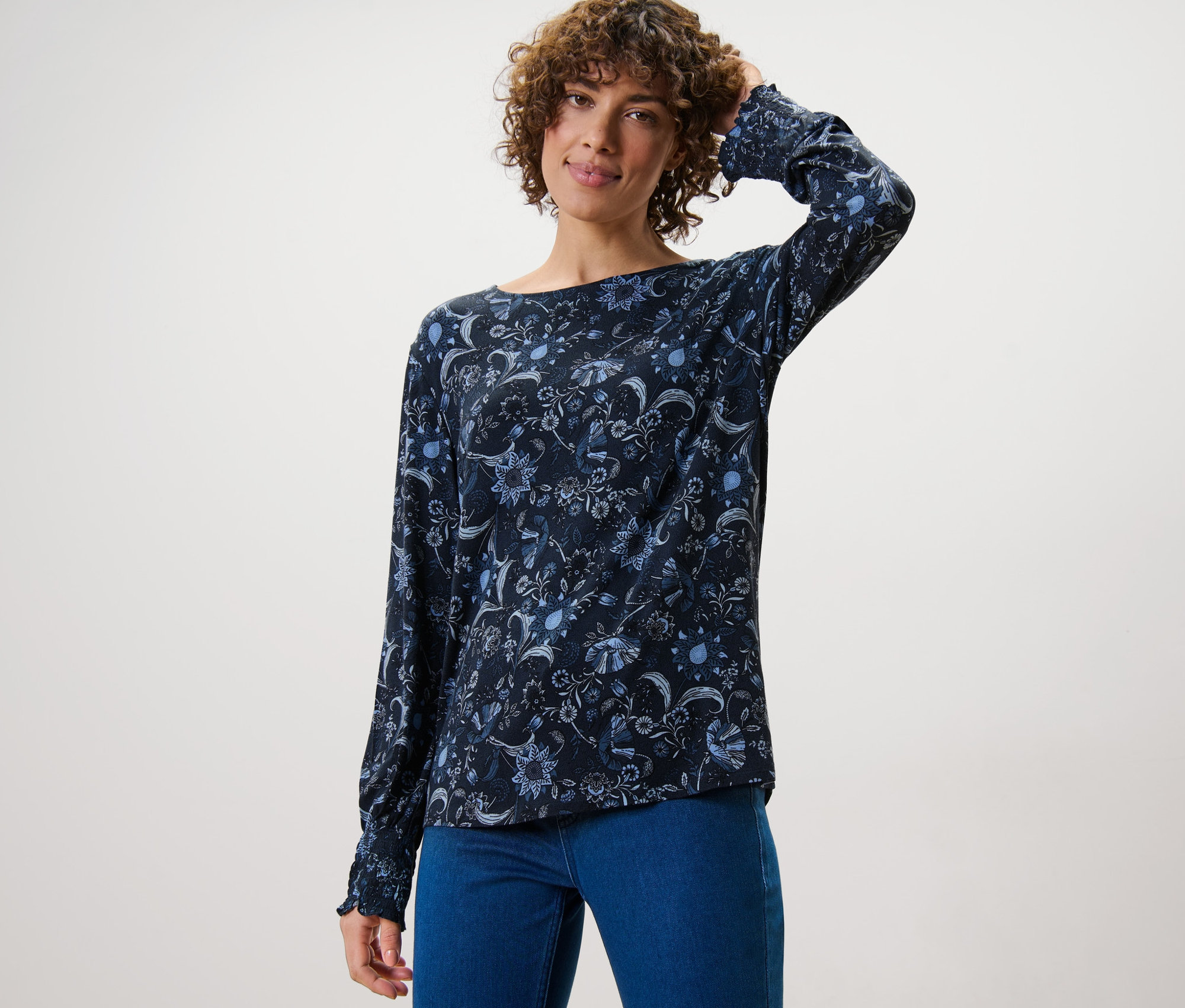 Kobieta pozuje w wzorzystej bluzce i dżinsach.