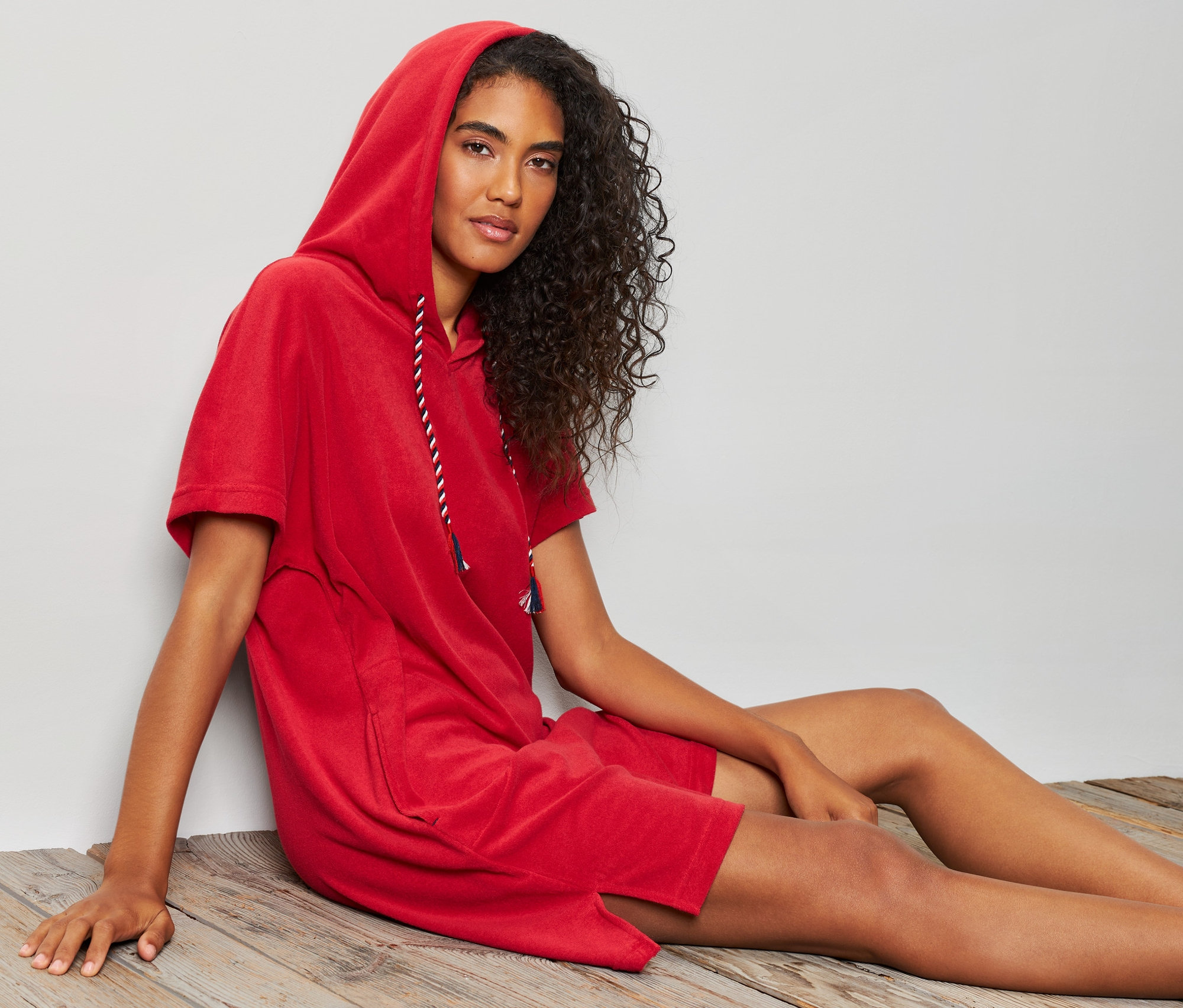 Kobieta siedzi na drewnianej podłodze w czerwonej sukience plażowej z tkaniny frotte.