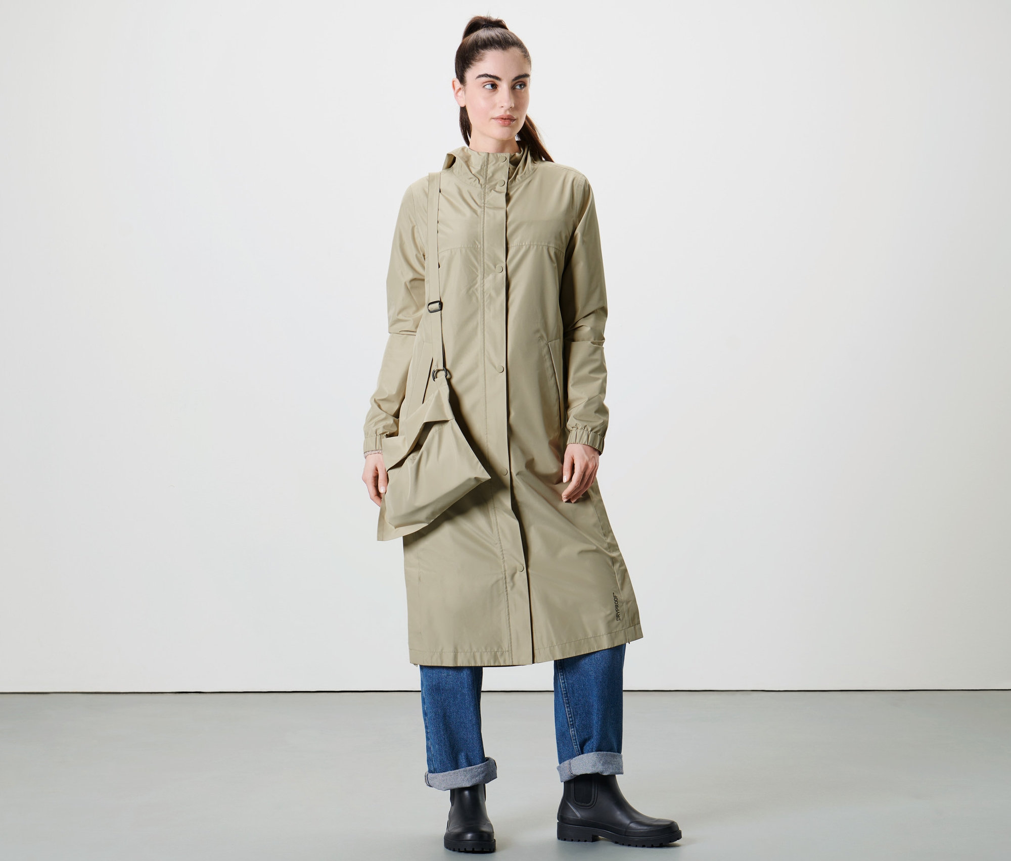Kobieta pozuje w studio w bardzo długim, beżowym płaszczu przeciwdeszczowym.