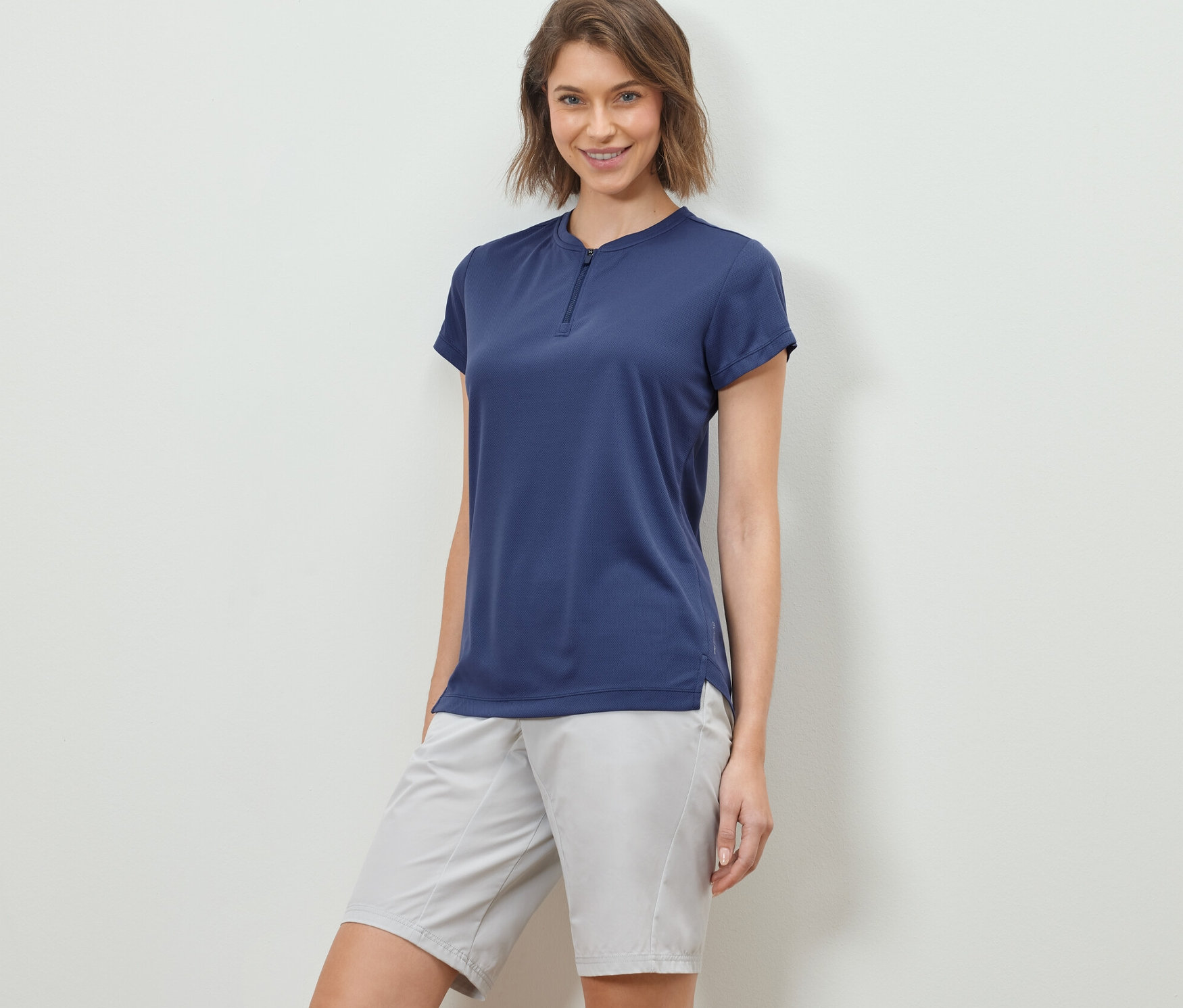 Kobieta pozuje w koszulce sportowej z krótkim zamkiem błyskawicznym i szortach.