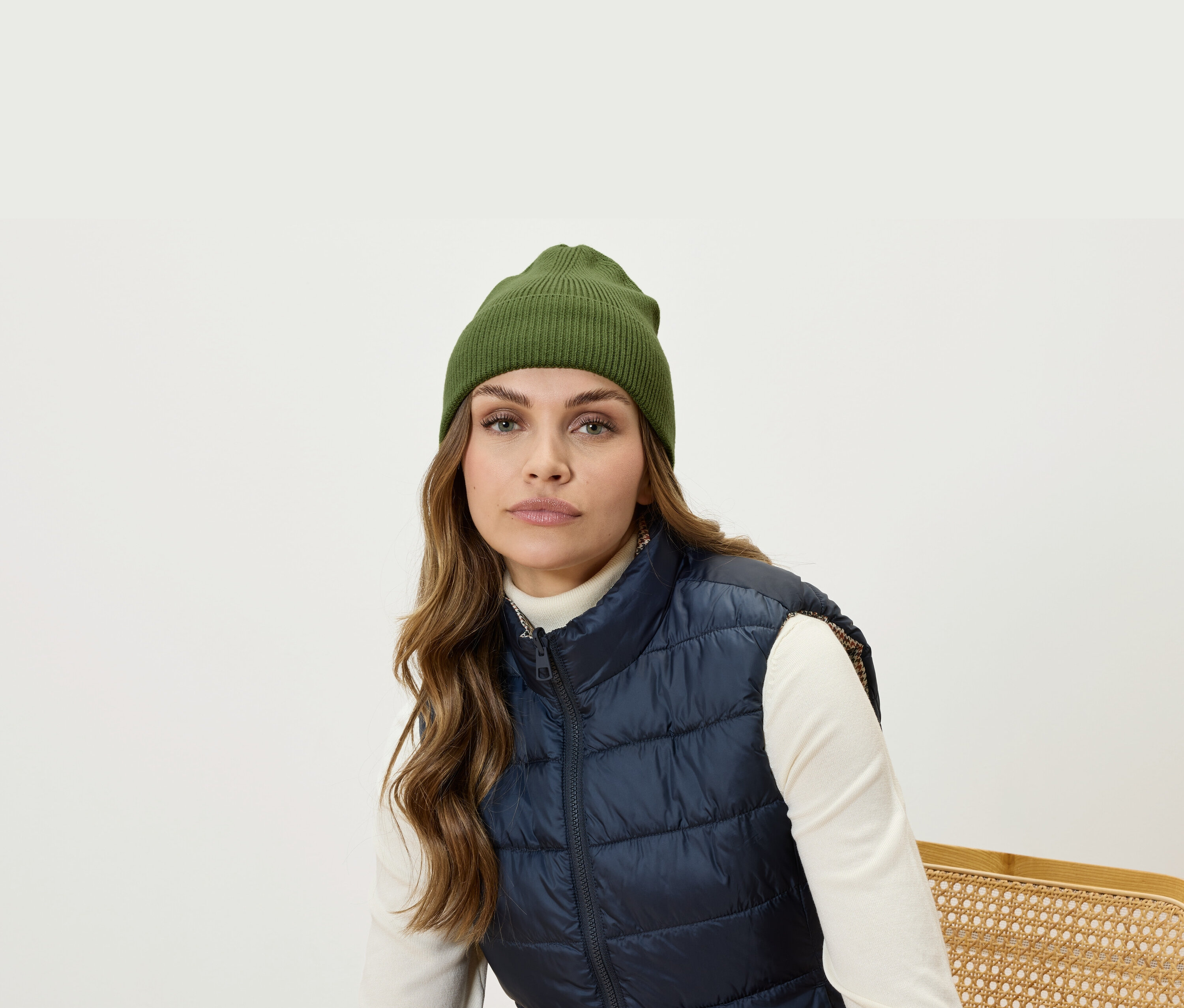 Portret kobiety o brązowych włosach w oliwkowej czapce i granatowej, pikowanej kamizelce.