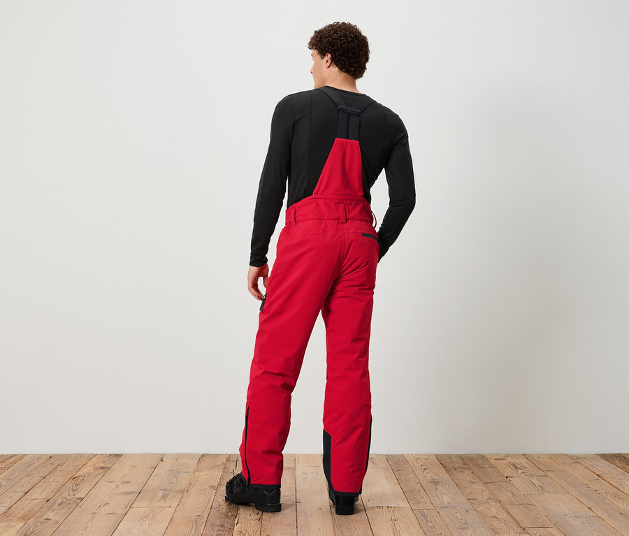 Mężczyzna tyłem do aparatu w czerwonych spodniach narciarskich na szelkach i czarnej koszulce.