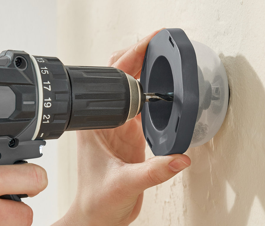 Osoba wierci wiertarką przez łapacz pyłu Bohrstaubfänger w ścianie.
