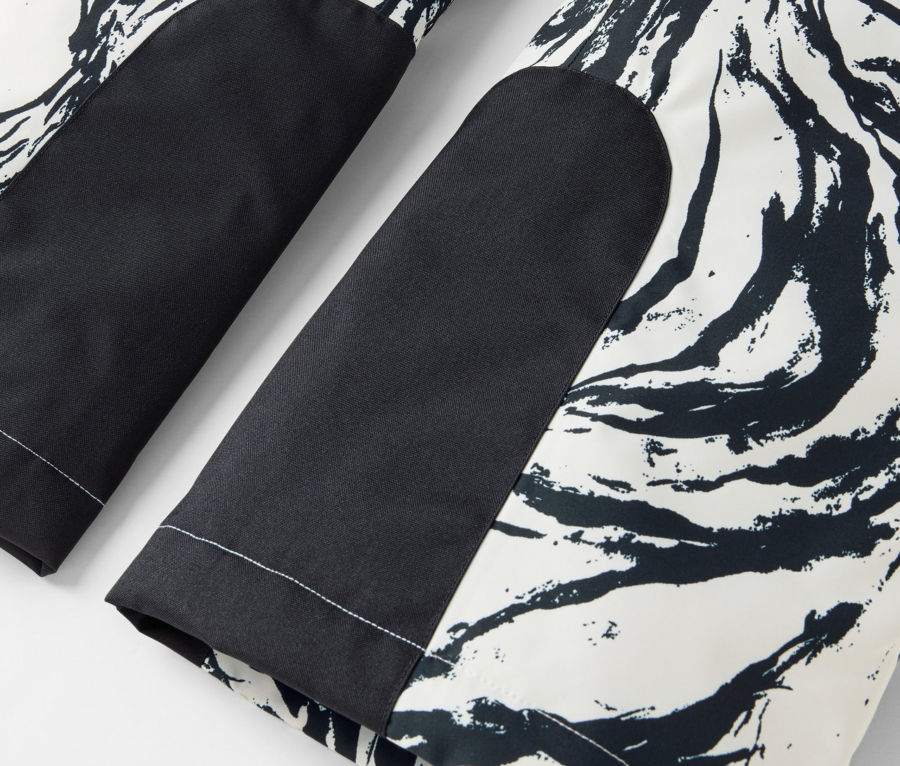 Szczegół czarno-białych spodni z abstrakcyjnym wzorem i czarnymi łatami na kolanach.