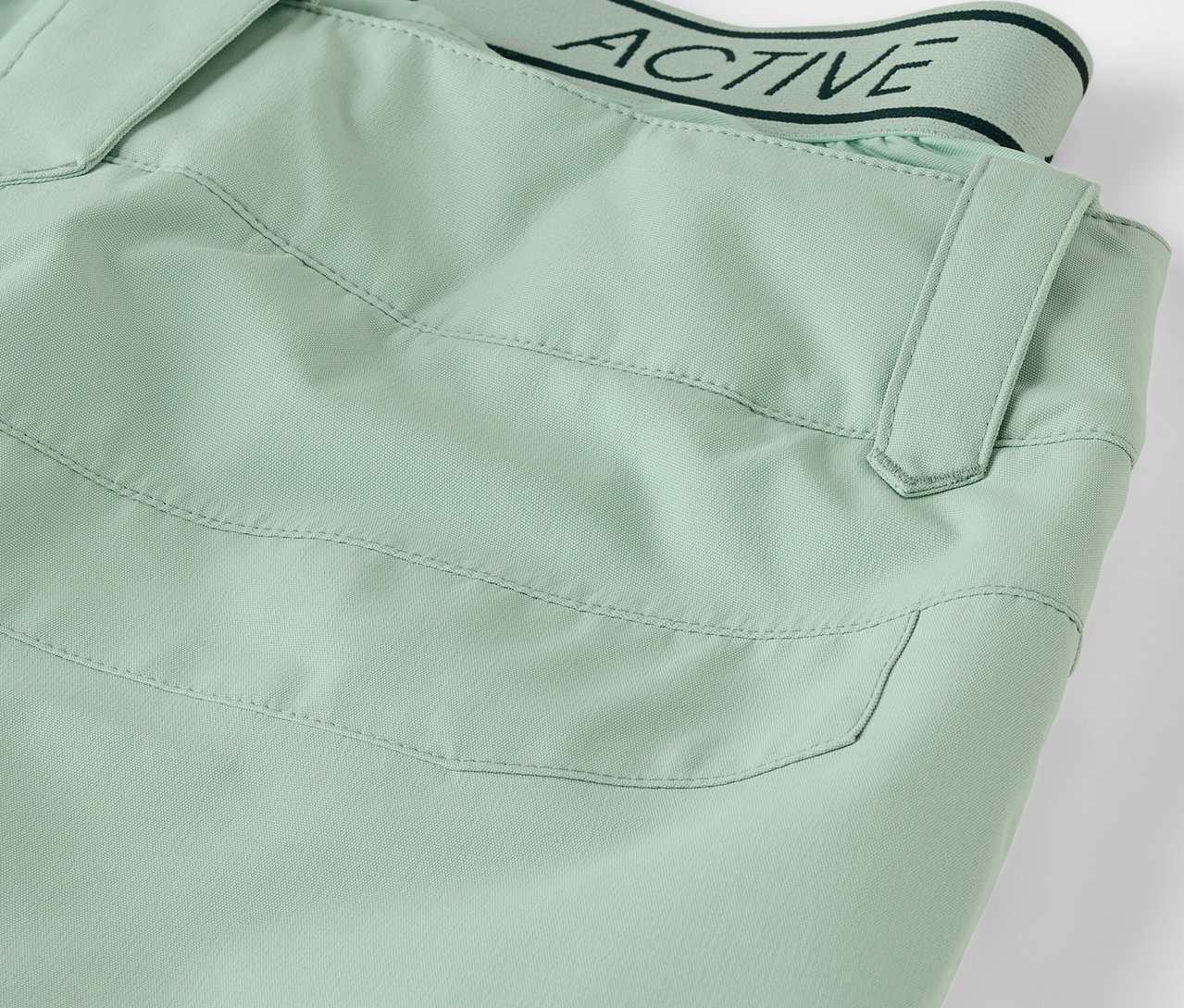 Szczegół jasnozielonych spodni z kieszenią i pasem z napisem ACTIVE.