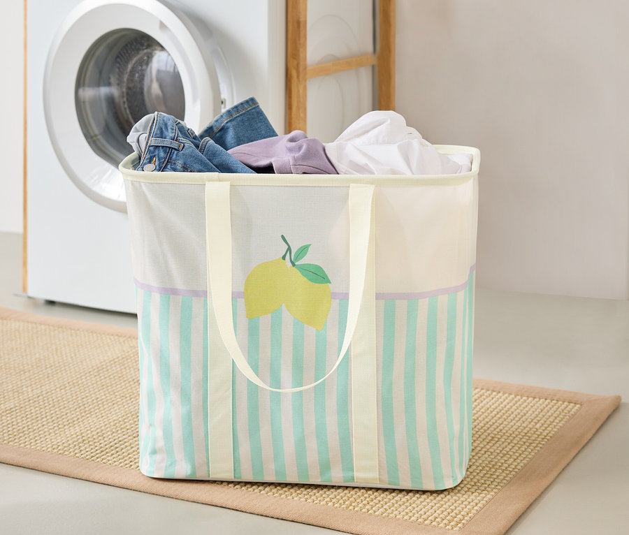 Kosz na pranie z motywem cytryny stoi na macie w pralni, w tle pralka i półka.