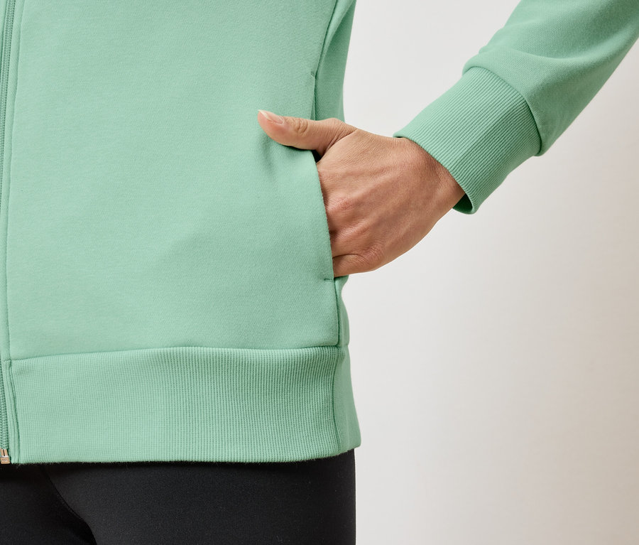 Zbliżenie na jasnozieloną damską bluzę z zamkiem błyskawicznym i ręką w kieszeni.